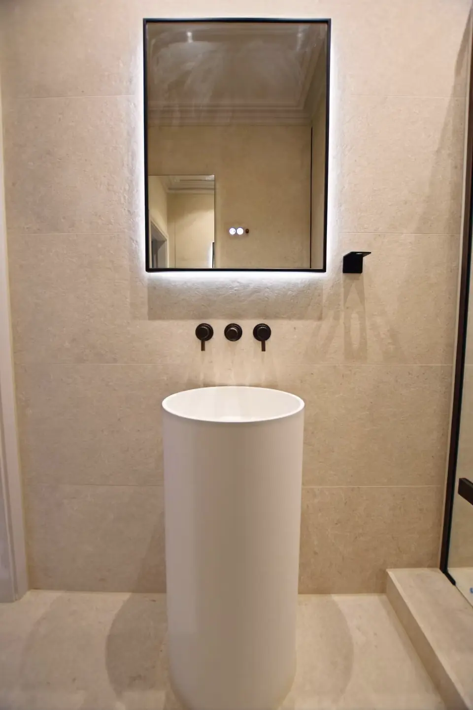 Luxury bathroom with cylinder pedestal basin, black-framed LED mirror and matte black fittings